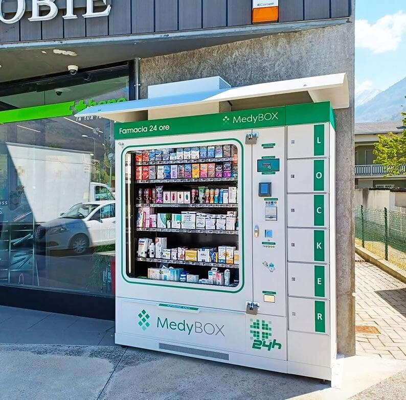 Outdoor MEDBOX pharmacy vending machine equipped with MdyLock add-on for secure pickup of pre-purchased products, including prescription medicines. Positioned outside a pharmacy, the machine offers a full array of products for customers to purchase directly from the sidewalk